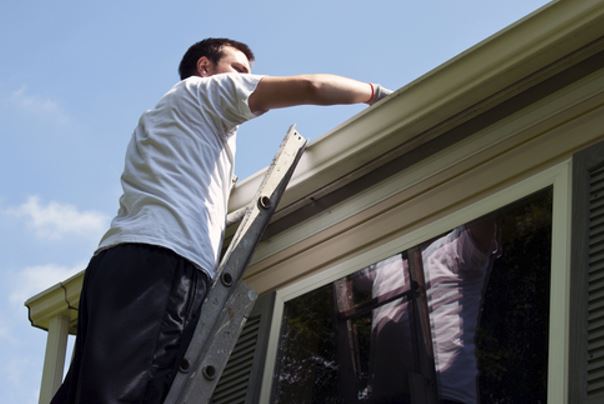 man cleaning gutters on ladder