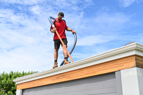 Professional Contractor Cleaning Gutters on Top of a Roof