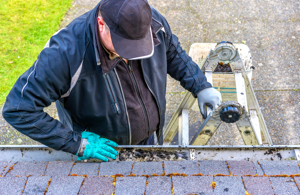 Man On Top of Ladder Cleaning Leaves Off Gutters